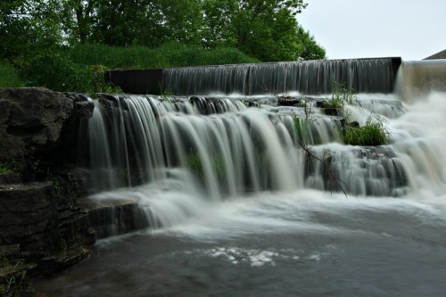 A serene waterfall cascading over rocks, surrounded by lush greenery and flowing into a calm body of water.