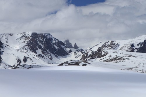 Snow-covered mountains under a cloudy sky, with a prominent peak in the distance.