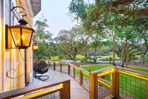 A wooden deck with a lantern overlooks a lush green landscape and trees by a calm waterway at dusk.