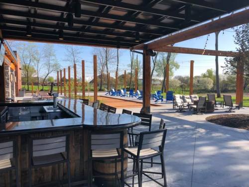 Outdoor bar area with seating, overlooking a patio with lounge chairs and trees in the background.