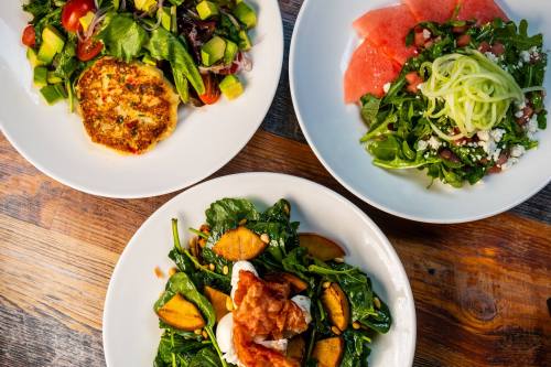 Three plates of fresh salads: one with greens and avocado, another with watermelon, and a third with spinach and peaches.