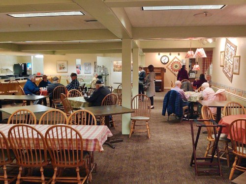 A cozy dining area with wooden tables and chairs, where people are seated and interacting in a warm atmosphere.