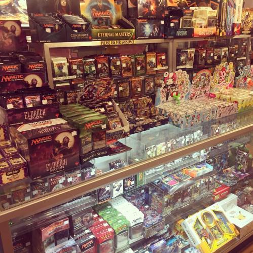 A display case filled with various collectible card game boxes and merchandise, including Magic: The Gathering products.
