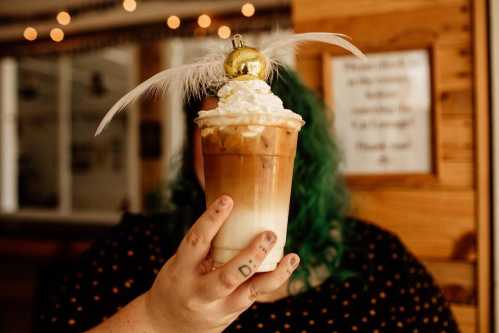 A person with green hair holds a festive iced coffee topped with whipped cream and a decorative ornament.