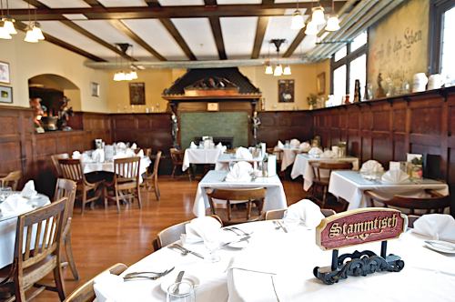 Cozy restaurant interior with wooden decor, tables set with white linens, and a sign reading "Stammtisch" in the foreground.