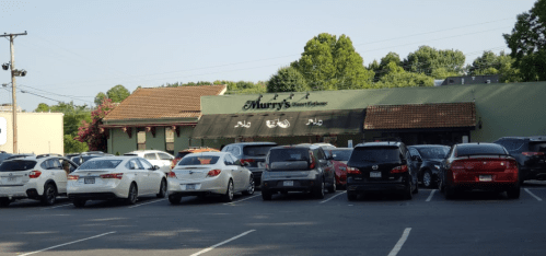 A parking lot filled with cars in front of a restaurant named "Murry's" surrounded by trees.