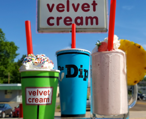 Three colorful milkshakes with whipped cream and sprinkles, in front of a sign that reads "velvet cream."