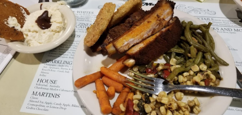 A plate with fried chicken, green beans, carrots, corn salad, and a side of mashed potatoes with gravy.