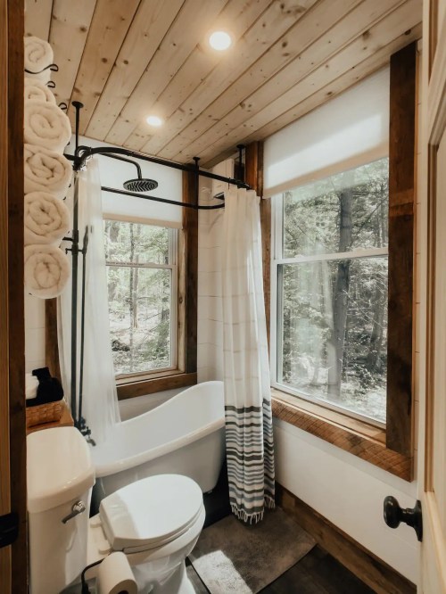 Cozy bathroom with a freestanding tub, shower curtain, and large windows overlooking a forested area.