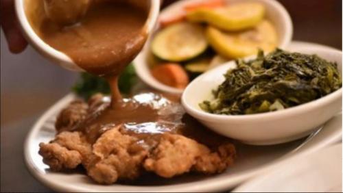 A plate of fried chicken topped with gravy, accompanied by greens and a side of mixed vegetables.