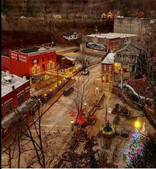 A charming town square decorated for the holidays, featuring lights, a Christmas tree, and historic buildings.