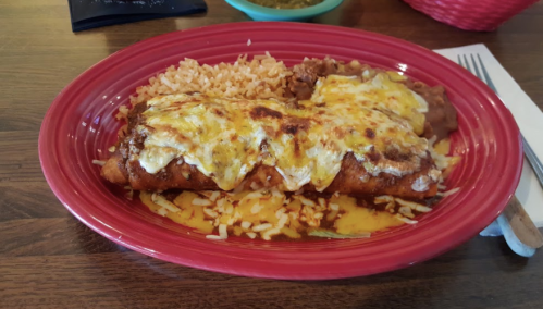 A red plate with enchiladas topped with cheese, served with rice and refried beans on the side.