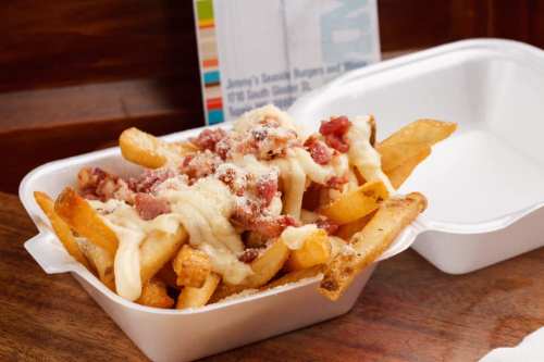A takeout container filled with loaded fries topped with cheese and bacon bits.