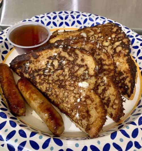 Plate of French toast with syrup and two sausage links on the side.
