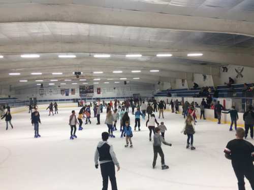 A busy ice skating rink filled with people skating and enjoying the activity under bright lights.