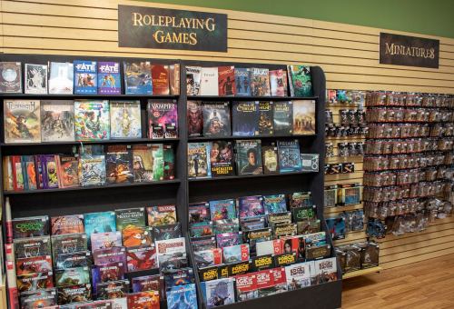 A game store display featuring shelves of roleplaying games and miniatures against a green wall.