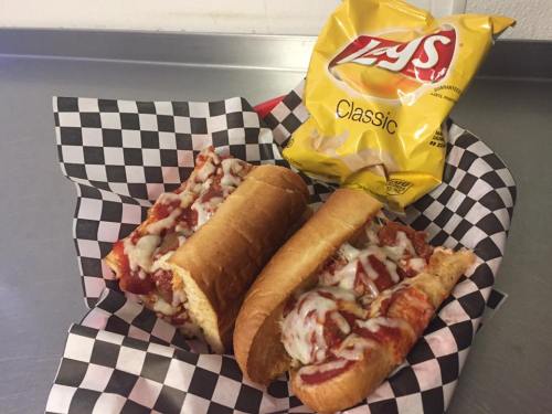 Two cheesy meatball subs on a checkered paper plate, accompanied by a bag of Lay's Classic chips.