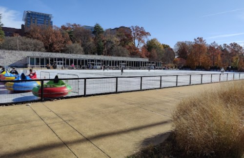 A winter scene with people ice skating and colorful bumper cars on a rink, surrounded by autumn trees and buildings.