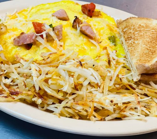 A plate of fluffy omelette topped with diced tomatoes and ham, served with crispy hash browns and toasted bread.