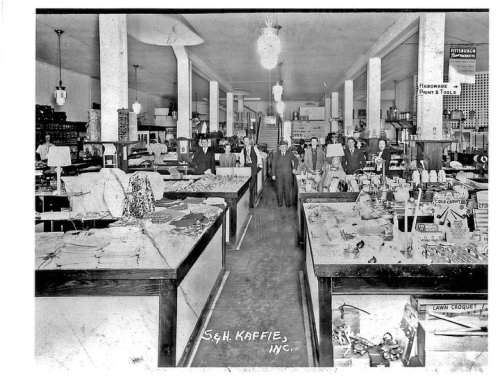 Historic black-and-white photo of a busy store interior with shelves of goods and customers browsing.