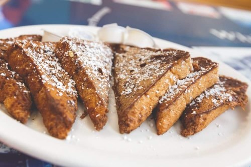 A plate of golden-brown French toast slices dusted with powdered sugar, served with a side of syrup.