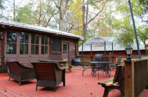 A cozy outdoor deck with seating, a dining table, and a gazebo, surrounded by trees in autumn foliage.