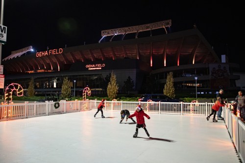 Children ice skate on a rink outside Geha Field, illuminated by festive lights at night.