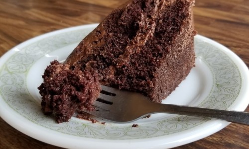 A slice of chocolate cake on a decorative plate, with a fork resting beside it.