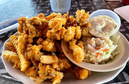 A plate of crispy fried seafood, including shrimp and fish, served with coleslaw and a side of dipping sauce.