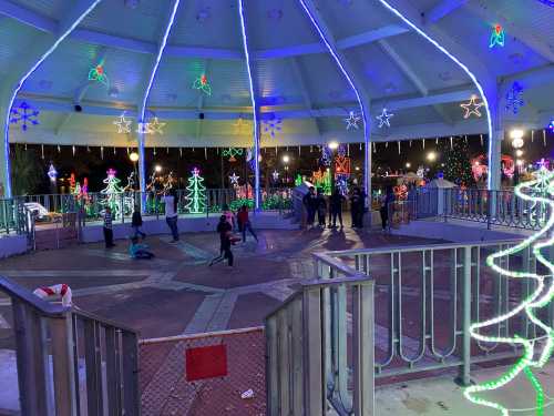 A festive gazebo decorated with colorful Christmas lights and trees, with people enjoying the holiday atmosphere.