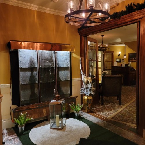 A cozy entryway featuring a water feature, plants, and a chandelier, leading to a warmly lit reception area.