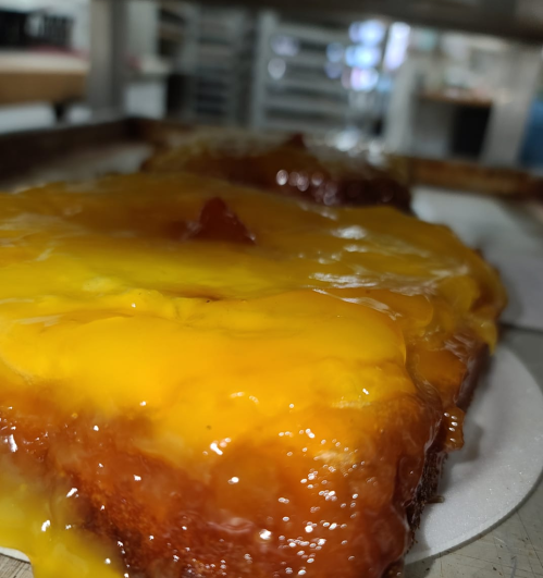 A close-up of a glossy, yellow dessert with a caramelized top, sitting on a baking tray in a kitchen setting.