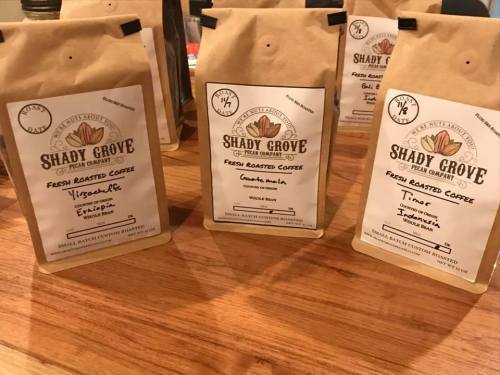 Bags of fresh roasted coffee from Shady Grove, labeled with origins like Ethiopia and Timor, displayed on a wooden surface.