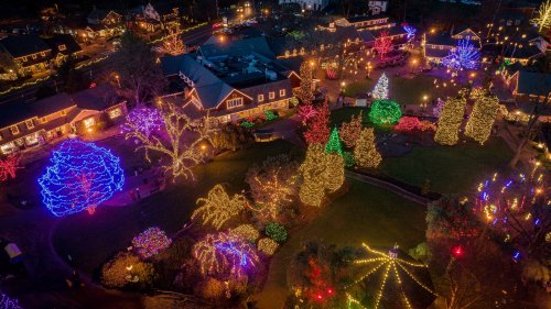 Aerial view of a festive display with colorful Christmas lights illuminating trees and buildings in a holiday setting.