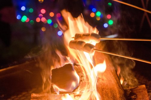 Marshmallows roasting over a vibrant campfire, with colorful lights blurred in the background.