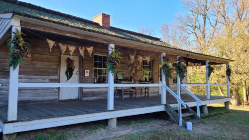 A rustic wooden house with a porch decorated for the holidays, featuring greenery and bunting.