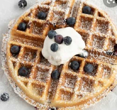 A golden waffle topped with whipped cream and fresh blueberries, dusted with powdered sugar.