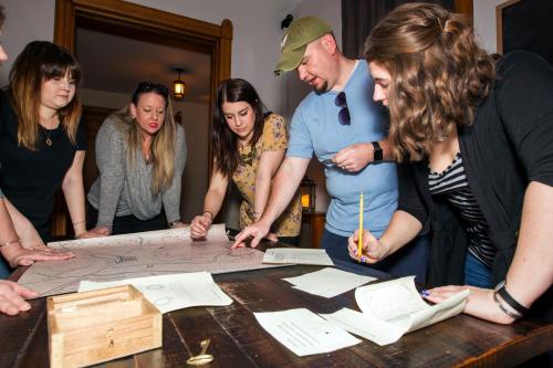 A group of six people gathered around a table, examining a large map and discussing plans.