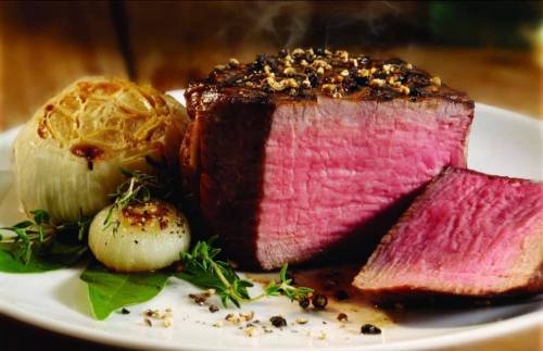 A perfectly cooked beef roast with a pink center, served with roasted onions and herbs on a white plate.