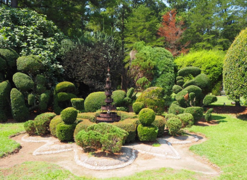 A beautifully landscaped garden featuring sculpted bushes and a central decorative structure surrounded by greenery.