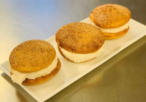 Three cream-filled pastries with a cinnamon sugar topping, arranged neatly on a white rectangular plate.