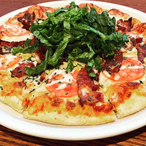 A pizza topped with cheese, pepperoni, and a generous serving of fresh greens on a white plate.