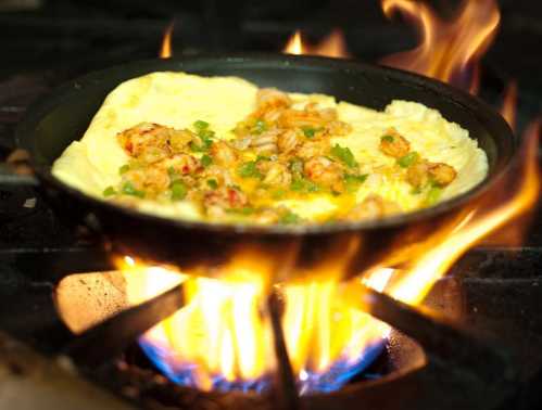 A sizzling omelette with shrimp and green onions cooking in a pan over an open flame.