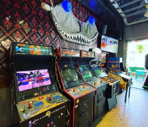 A row of classic arcade machines in a retro-themed gaming space, featuring colorful screens and vibrant decor.
