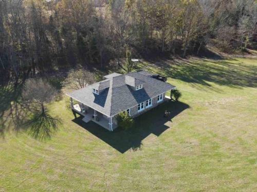 Aerial view of a single-story house surrounded by trees and a grassy field.