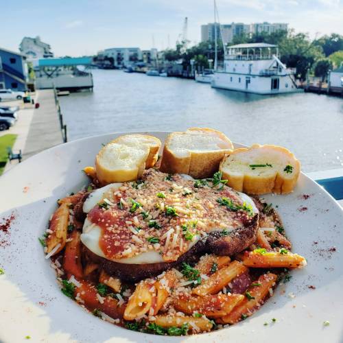 A plate of pasta topped with cheese and herbs, served with toasted bread, overlooking a scenic waterfront view.