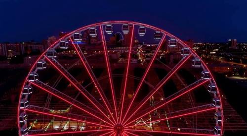 A brightly lit Ferris wheel at night, surrounded by city lights and a dark sky.