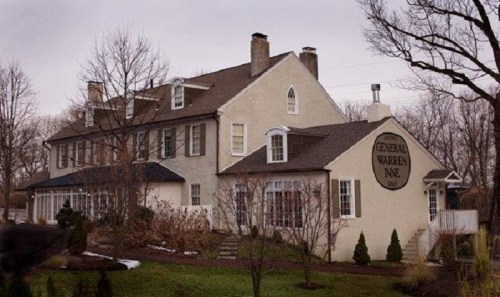 Historic building with a sign reading "General Warren Inn," featuring a mix of stone and siding, surrounded by trees.