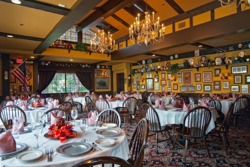 Elegant dining room with round tables set for a meal, adorned with pink napkins and decorative wall art.