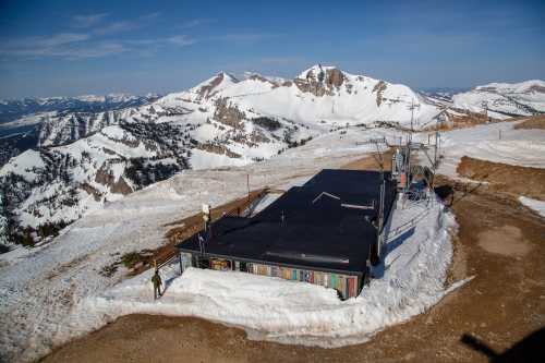 A mountain landscape with snow-covered peaks and a small building surrounded by snow on a rocky terrain.